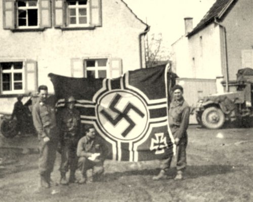 Photograph of four soldiers holding up a Nazi flag captured by Company B of the 56th Armored Inf.jpg